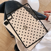 A beige protective case with black polka dots for an iPad Pro is shown resting on a person's jeans and white fabric.
