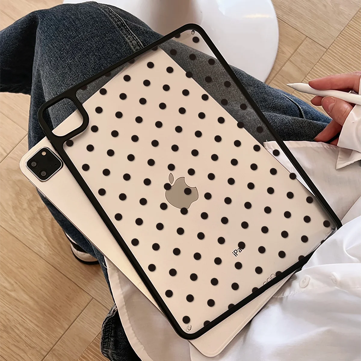 A beige protective case with black polka dots for an iPad Pro is shown resting on a person's jeans and white fabric.