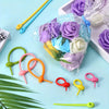 A collection of silicone cable organizers in various colors and a bouquet of purple roses are displayed on a light blue surfa