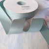 Roll of matte finish satin ribbon in sage green color with a white label visible.