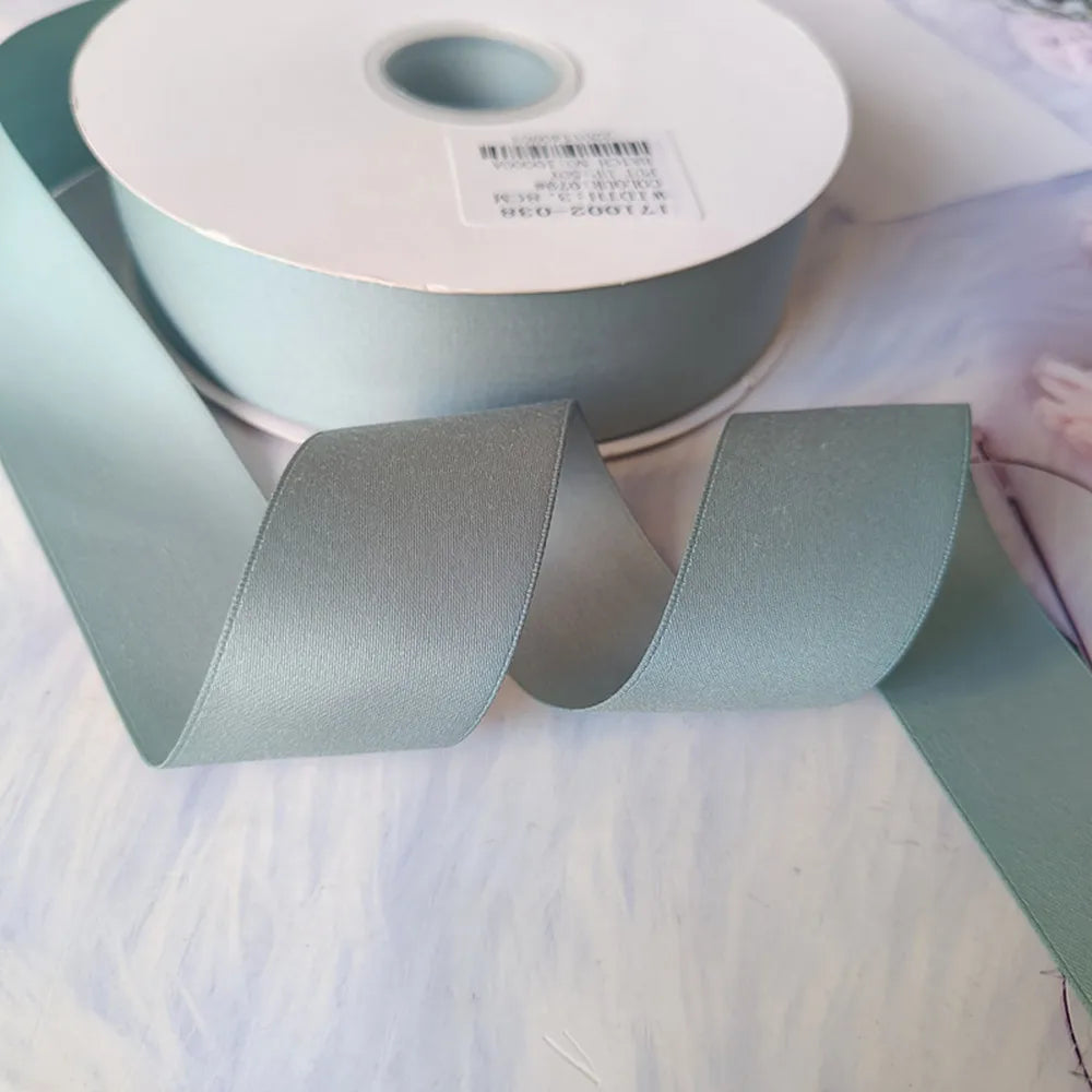 Roll of matte finish satin ribbon in sage green color with a white label visible.