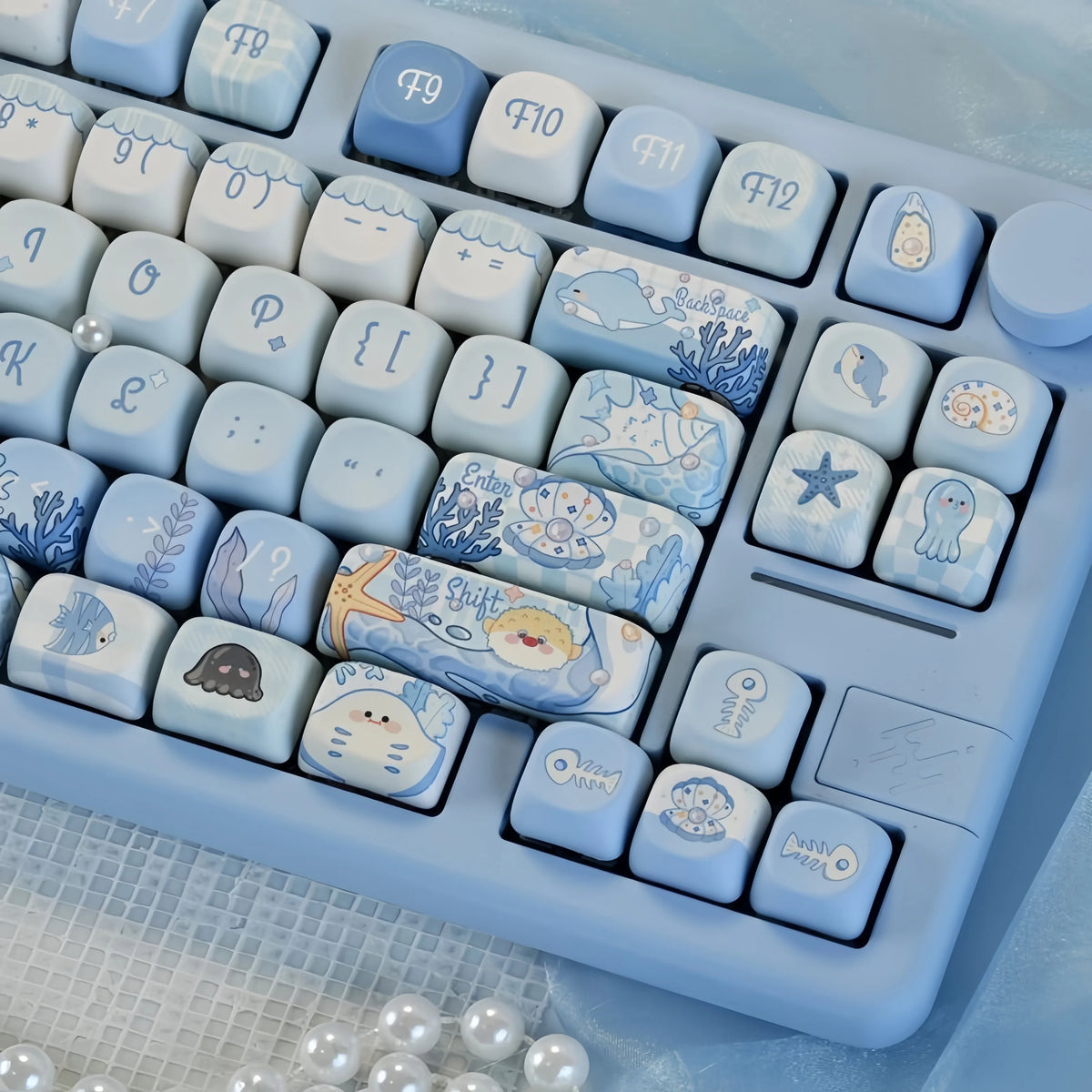 A close-up view of blue sea themed PBT keycaps for a mechanical keyboard arranged in a tray.