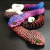 A collection of colorful, textured snake figurines made from yarn or fiber art displayed on a dark surface.