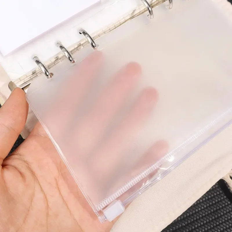 A hand holds a clear PVC zipper binder with pockets for cash and small items.