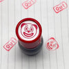 A red rubber stamp with a funny meme face design is shown on a white surface.