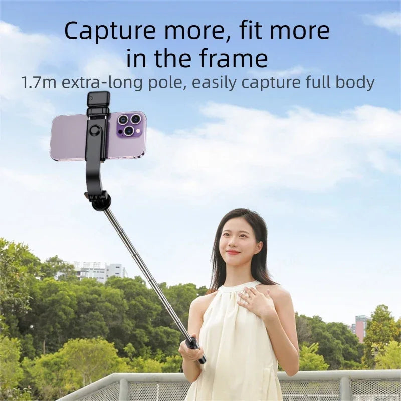 A woman holding an ultra-long selfie stick with a smartphone attached, outdoors against a green background.