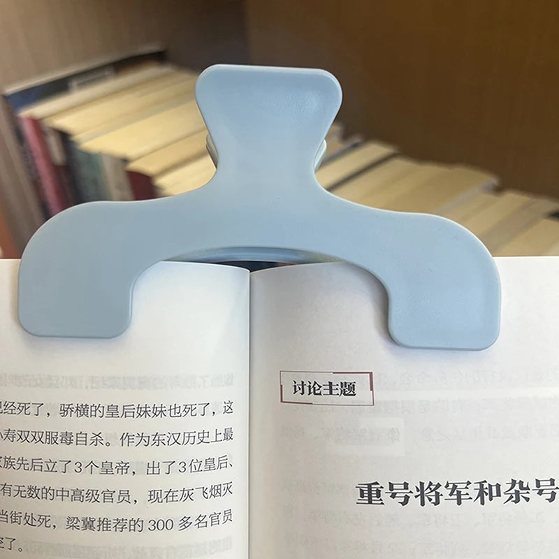 A close-up of a light blue book page clip used to hold open a page in a book.