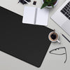 A black anti-slip rubber mouse pad is shown on a desk next to a laptop, notebook, and pen.