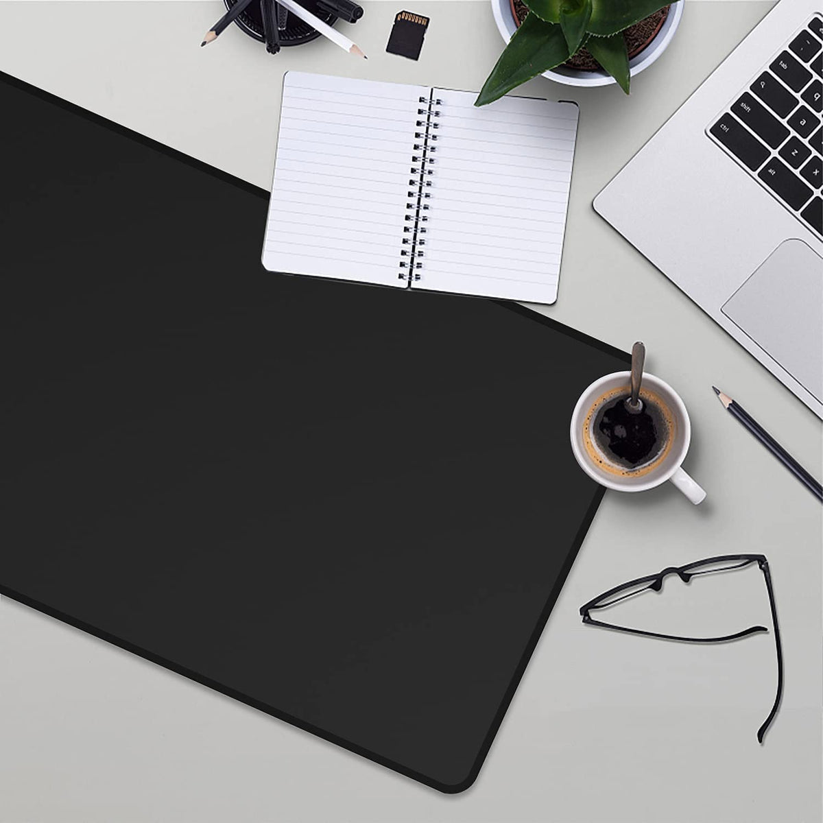 A black anti-slip rubber mouse pad is shown on a desk next to a laptop, notebook, and pen.