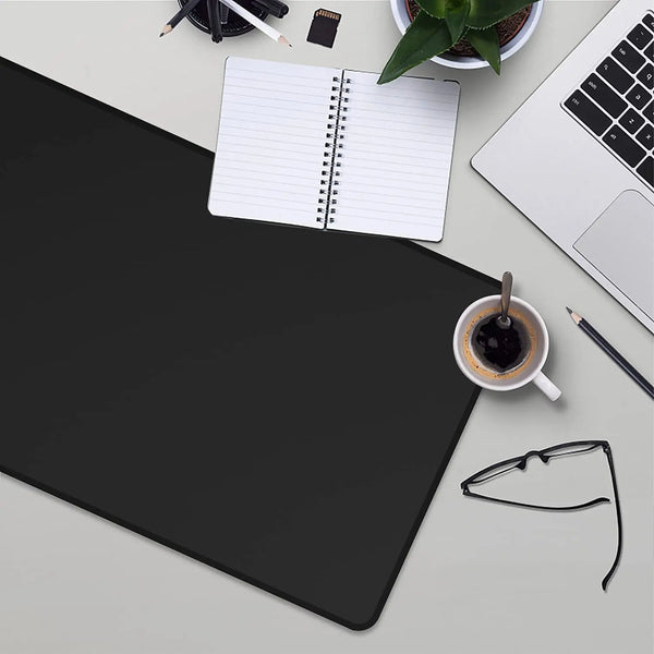 A black anti-slip rubber mouse pad is shown on a desk with a notebook, a laptop, and a cup of coffee.