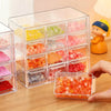 A clear acrylic storage box filled with colorful beads and stacked compartments, being held by a hand.