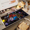 A dark mouse pad featuring various cartoon characters and designs, displayed next to a monitor.