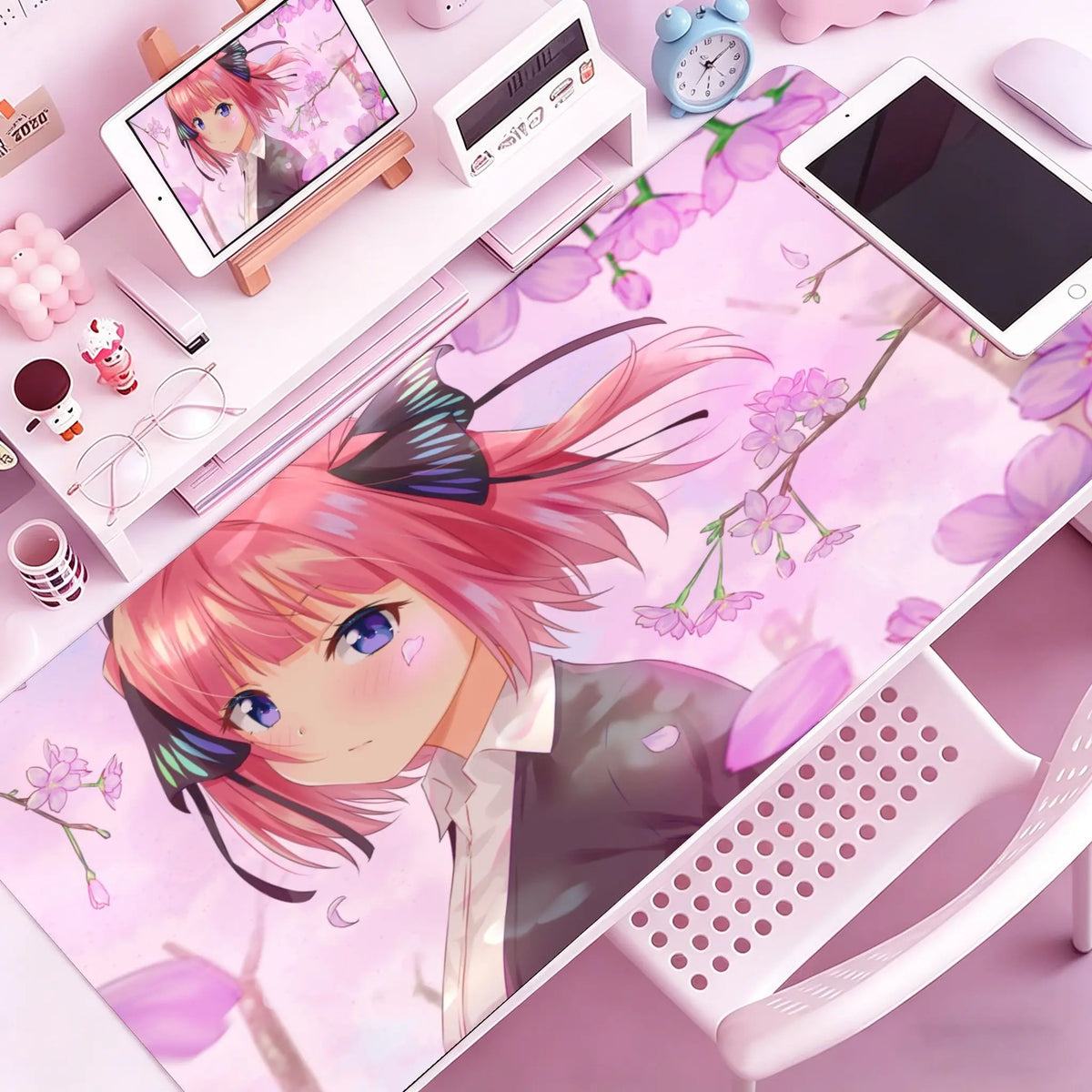 A pink anime character illustration on a large pink mouse pad with floral designs, next to a white mouse and clock.