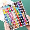 A palette of solid watercolor paints in various colors is held by a hand against a green background.