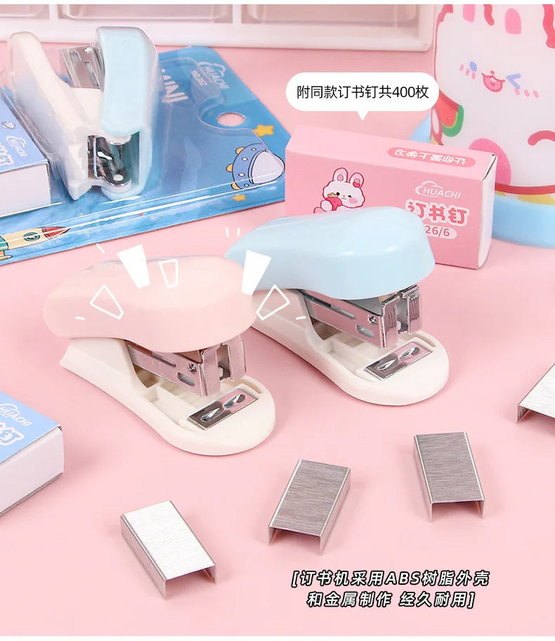 A set of pink and blue cartoon mini staplers for students and office use displayed on a pink background.