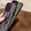 A close-up of a dark gray phone case featuring a black spider web design, shown on a wooden surface.