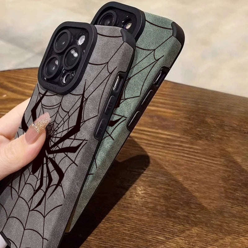 A close-up of a dark gray phone case featuring a black spider web design, shown on a wooden surface.