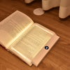 A rechargeable acrylic book night light with a timer resting on a wooden surface.
