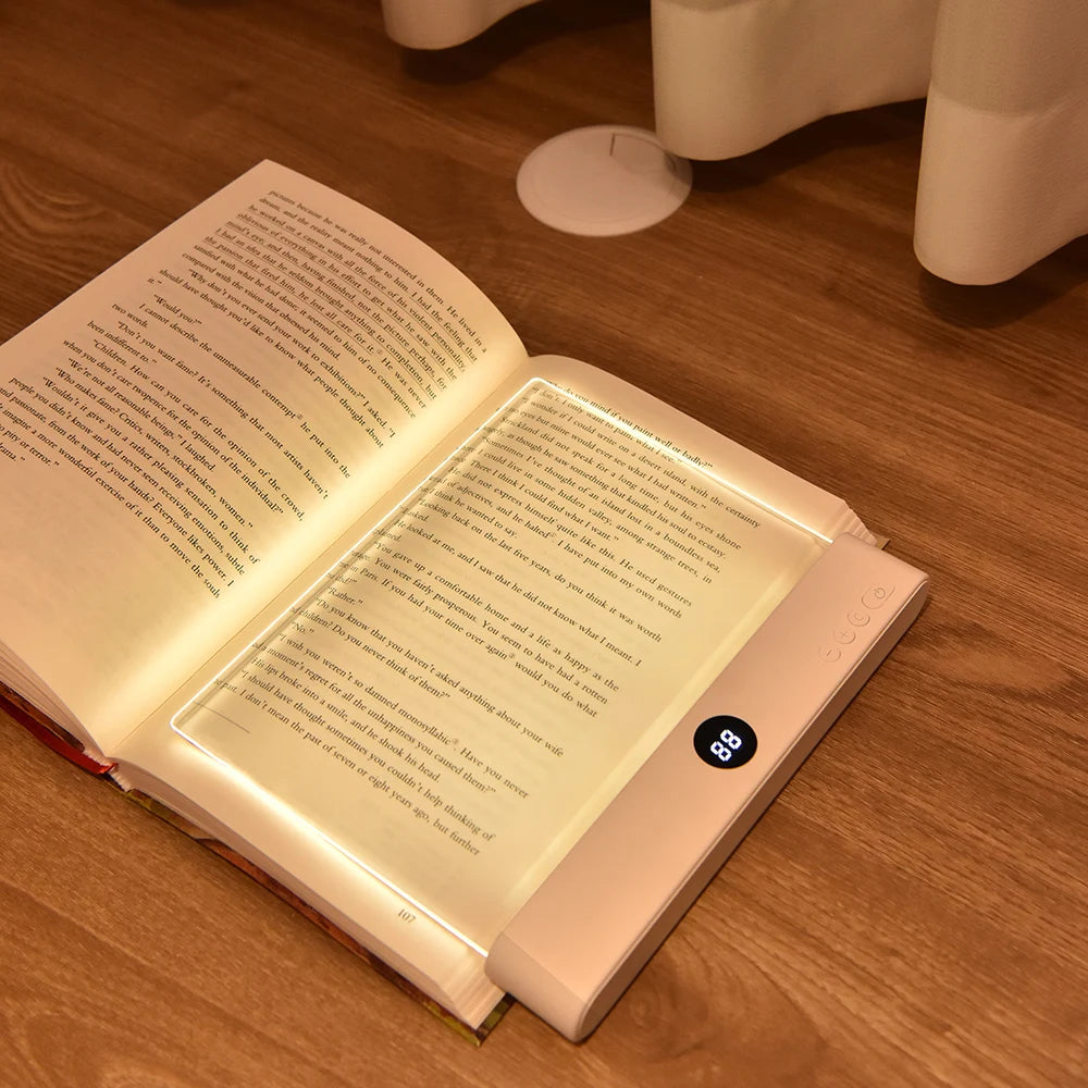 A rechargeable acrylic book night light with a timer resting on a wooden surface.