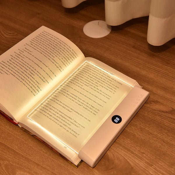 A rechargeable acrylic book night light with a timer resting on a wooden surface.
