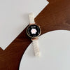A white resin beaded watch with a gold-toned case and white strap resting on a brown wooden surface.