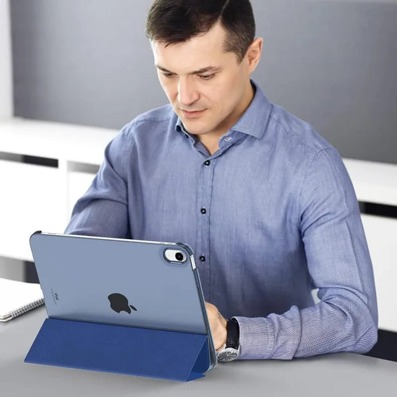 A man is using a slim blue stand case for an iPad on a desk.