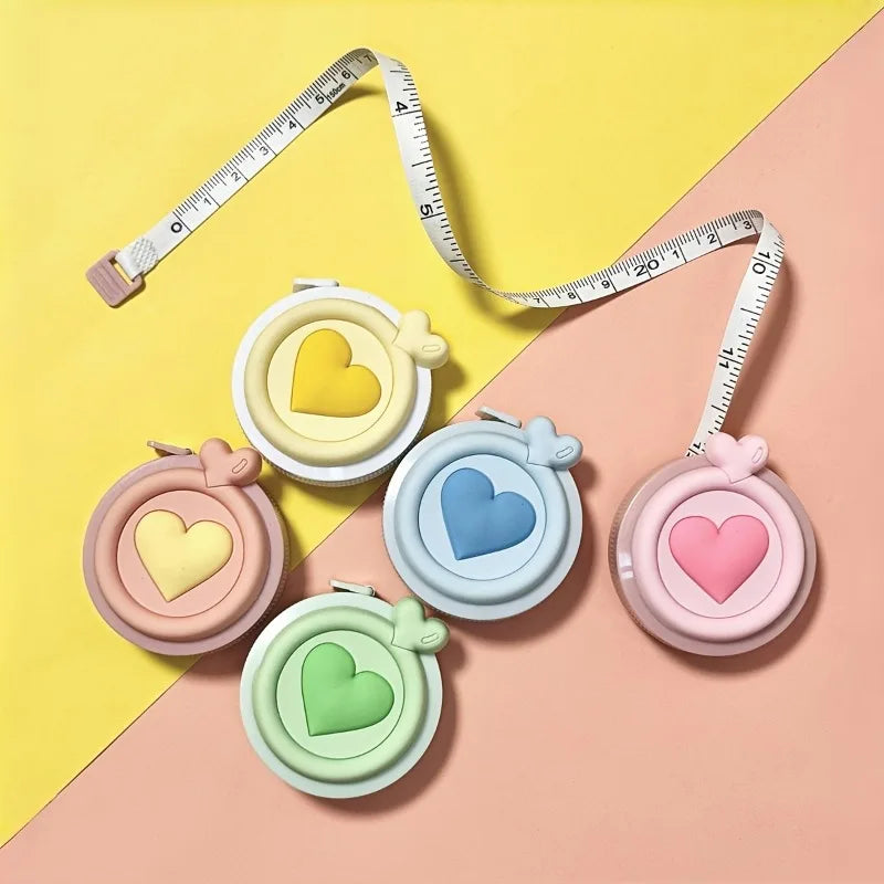 Un juego de cintas métricas en forma de corazón y una regla exhibidos sobre un fondo rosa.