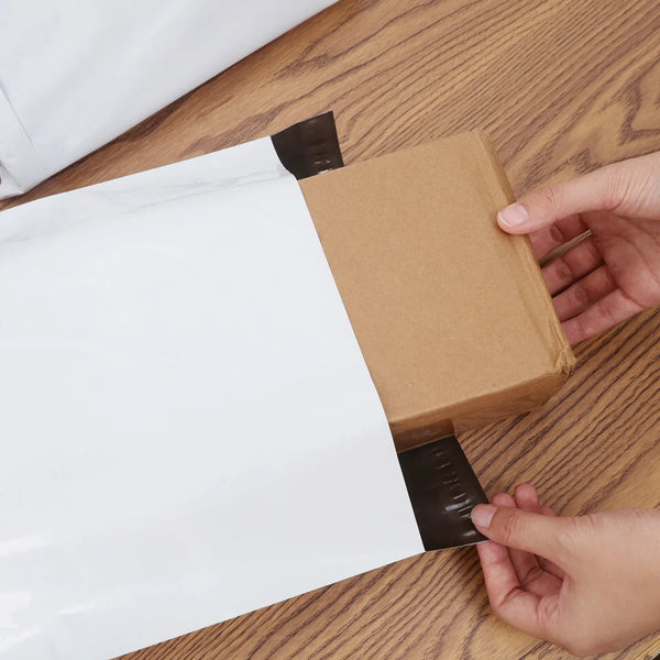 Hände versiegeln eine braune Kartonbox mit schwarzem Klebeband und weißem Papier auf einer Holzoberfläche.