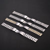 Several stainless steel watch bands with folding safety clasps laid diagonally on a dark surface.