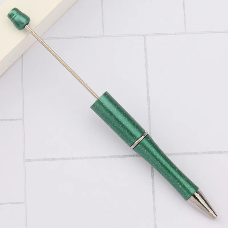 A green DIY beadable pen with a gold tip resting on a white surface.