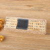 A wooden stamp seal set with monthly and weekly labels arranged in a rectangular box on a light wooden surface.