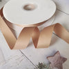 Roll of matte finish satin ribbon in a nude color lying on a white wooden surface.