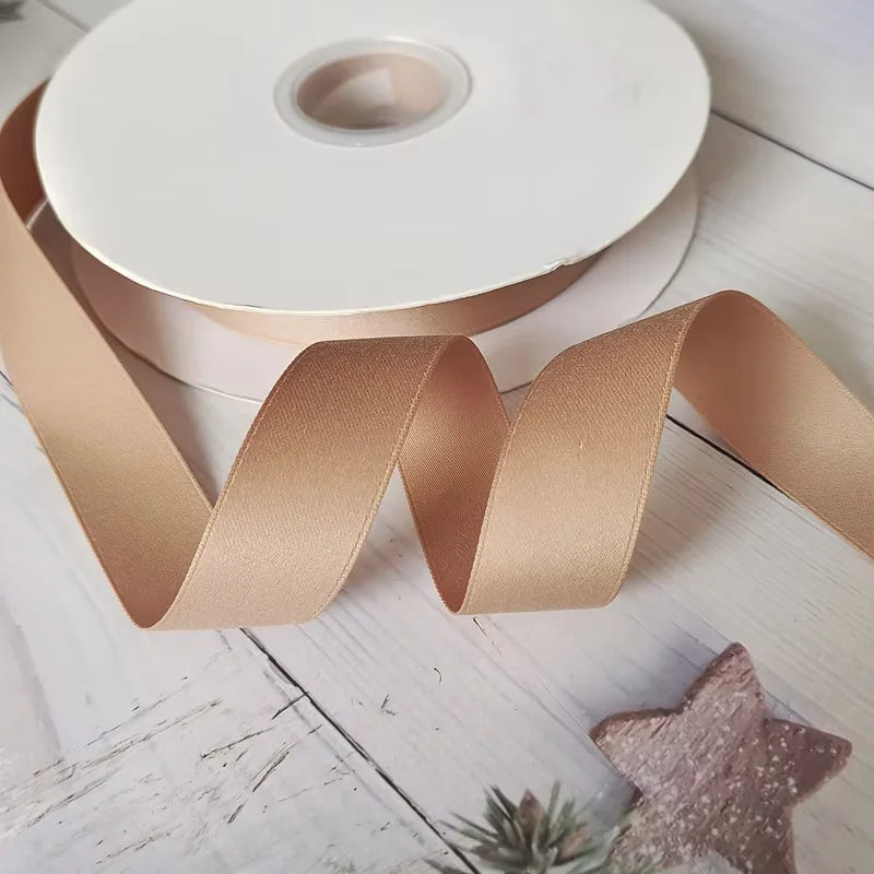 Roll of matte finish satin ribbon in a nude color lying on a white wooden surface.