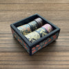 A set of metallic gold washi tape rolls in a dark box, displayed on a wooden surface.