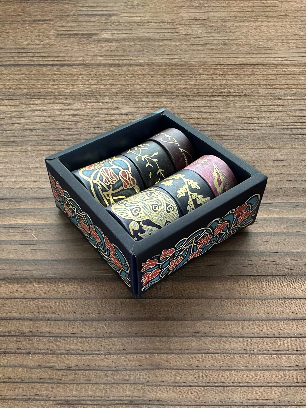 A set of metallic gold washi tape rolls in a dark box, displayed on a wooden surface.