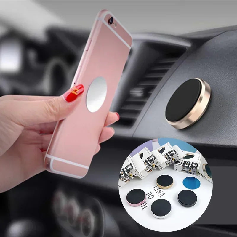 A hand holds a pink smartphone attached to a magnetic mount designed for a car dashboard.
