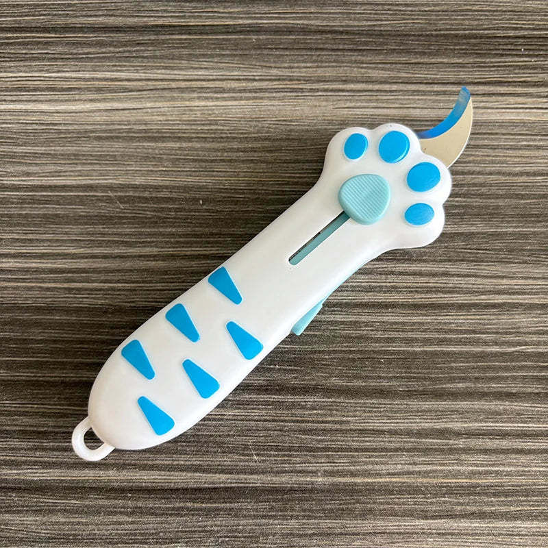 A white retractable cat paw utility knife with blue accents is shown on a gray wooden surface.