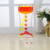 A glass hourglass filled with colored liquid, showing a flow of red, orange, and yellow droplets.