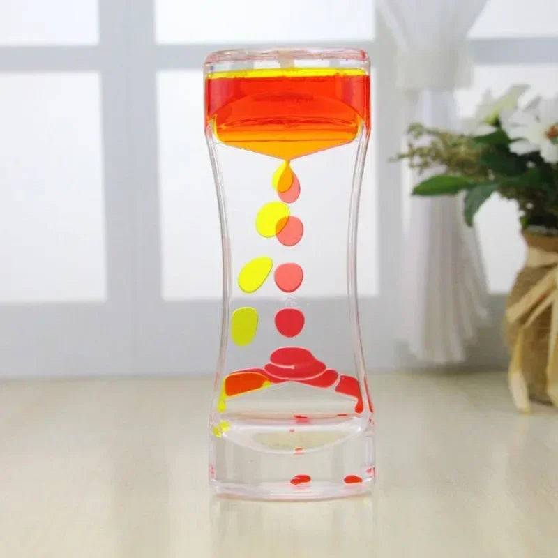 A glass hourglass filled with colored liquid, showing a flow of red, orange, and yellow droplets.