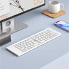A white foldable Bluetooth keyboard is shown next to a laptop screen and a smartphone on a light gray surface.