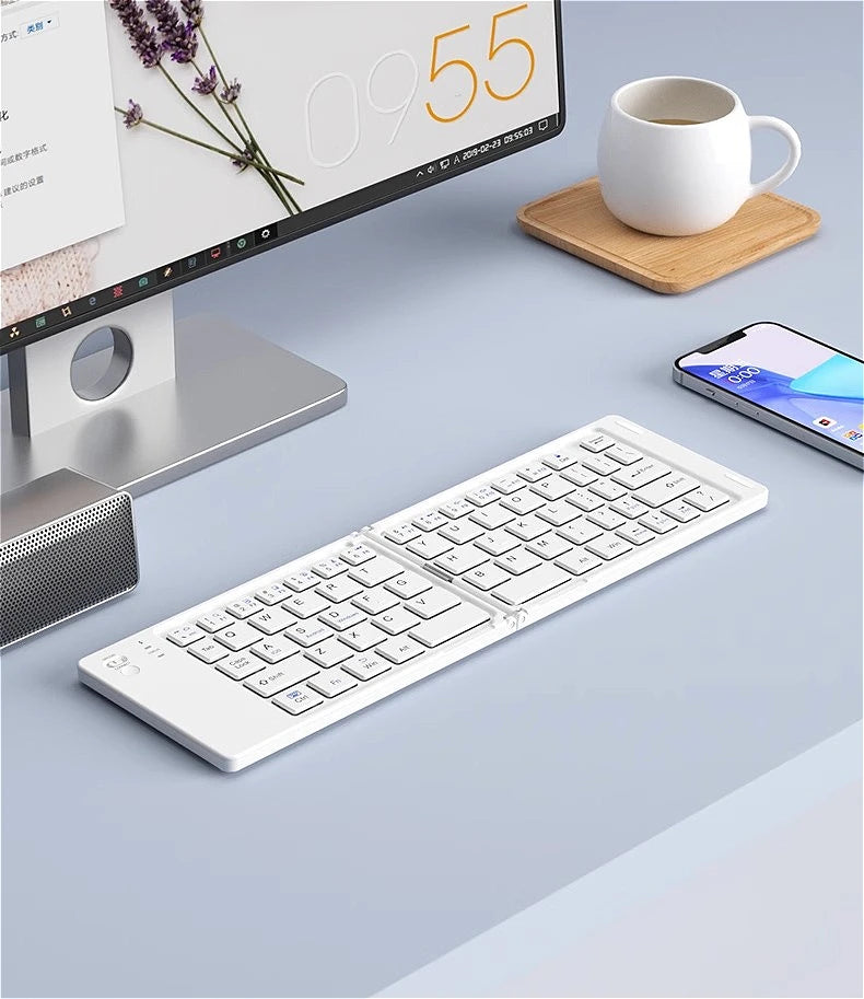 A white foldable Bluetooth keyboard is shown next to a laptop screen and a smartphone on a light gray surface.