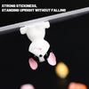 A white and black rabbit-shaped double-sided adhesive fixer pad is suspended above a dark surface.