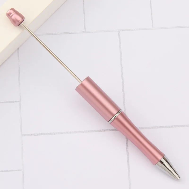 A pink DIY beadable pen set with a silver tip and gold accents resting on a white surface.