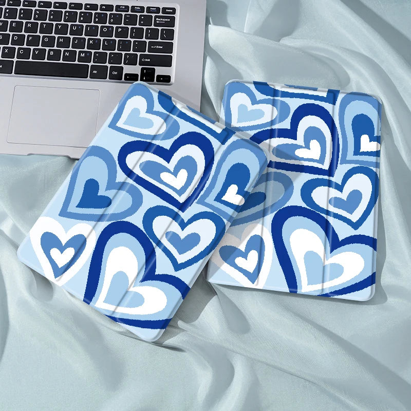 A blue and white patterned heart-themed iPad case with a pencil holder lying on a light blue fabric.