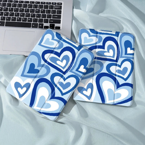 A blue and white patterned heart-themed iPad case with a pencil holder lying on a light blue fabric.