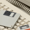 A silver M.2 NVMe SSD in an enclosure is shown resting on a grid of plastic blocks next to a coiled cable.