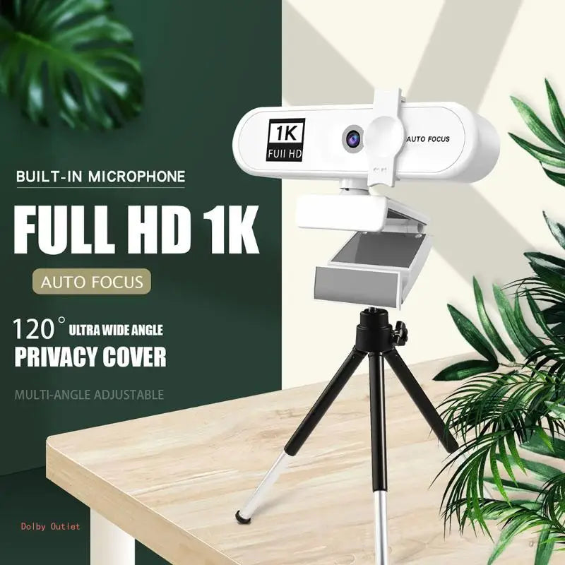Webcam autofocus HD blanche montée sur trépied, devant un fond de plante verte.