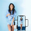 A woman is using an extendable Bluetooth selfie stick with a fill light to take a mirror selfie.