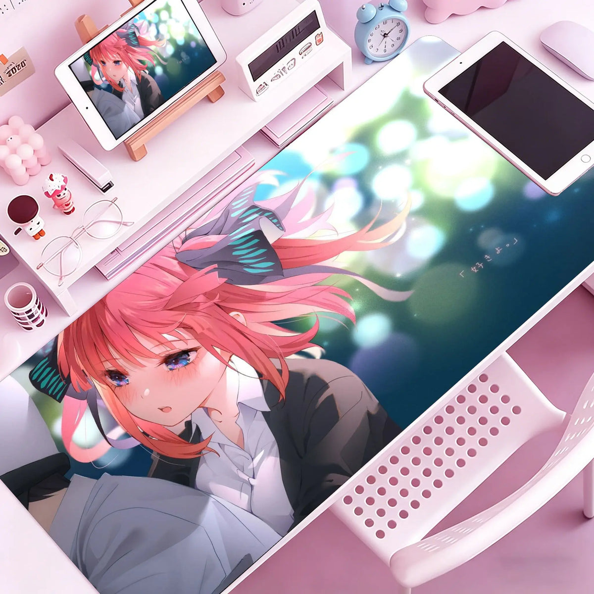 A vibrant anime illustration of a pink-haired character on a mouse pad and desk mat with surrounding office supplies.