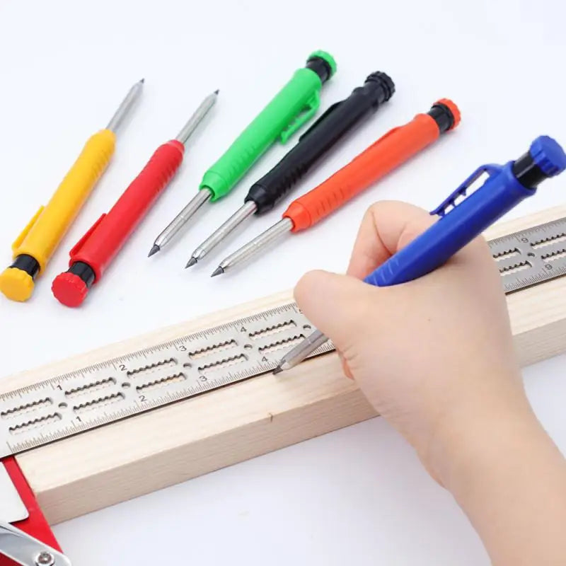 A hand holds a set of colored precision mechanical drawing pencils resting on a wooden ruler.